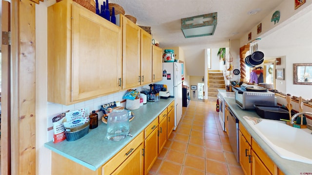 kitchen with light tile patterned floors, a sink, freestanding refrigerator, stainless steel dishwasher, and decorative backsplash