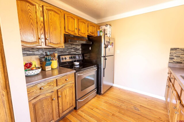 107 Shavano Dr Unit A1, Gunnison, CO 81230 - kitchen with baseboards, appliances with stainless steel finishes, under cabinet range hood, light wood finished floors, and decorative backsplash