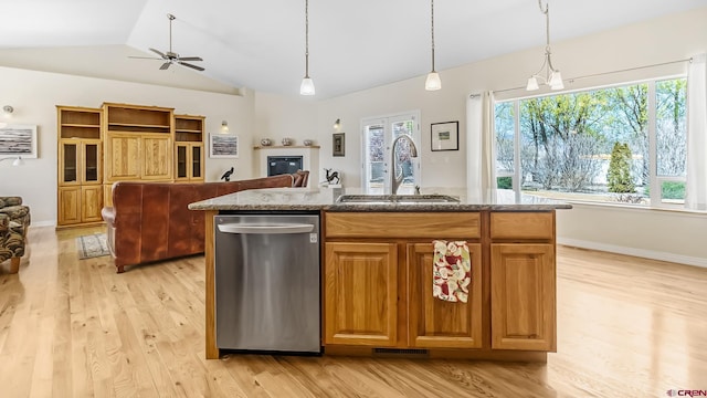 kitchen with a sink, light wood-style floors, a center island with sink, stone counters, and stainless steel dishwasher