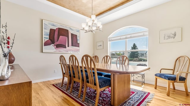 dining room with a chandelier, a raised ceiling, baseboards, and wood finished floors