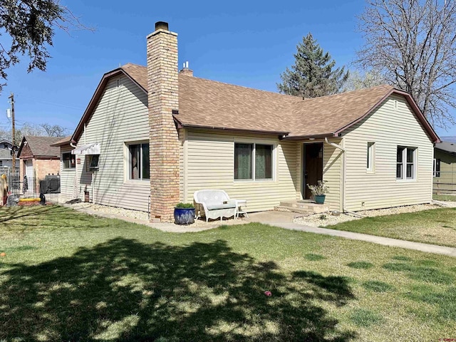 rear view of property featuring roof with shingles, a lawn, and a chimney