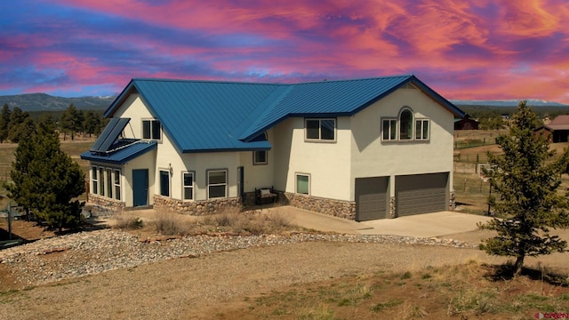 rear view of property featuring stone siding, metal roof, a garage, stucco siding, and driveway