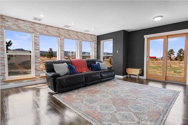living area featuring brick wall, visible vents, baseboards, and wood finished floors