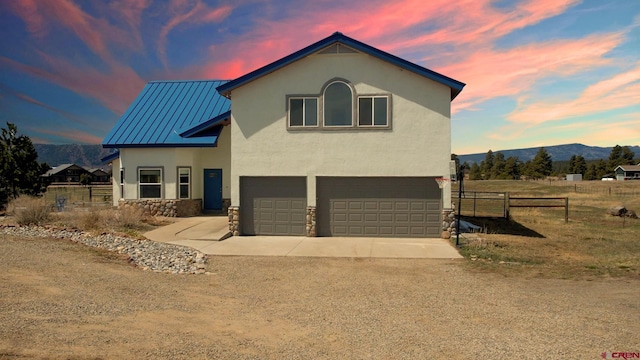 view of front facade with a mountain view, driveway, an attached garage, a standing seam roof, and fence
