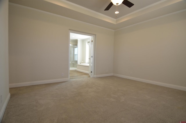 empty room with baseboards, a raised ceiling, ceiling fan, crown molding, and light carpet