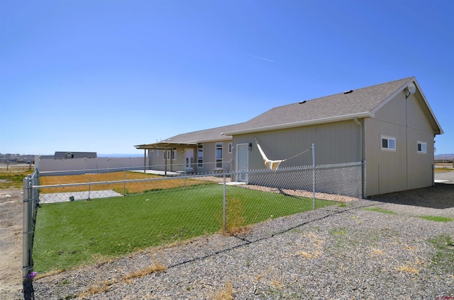 rear view of property featuring fence, a shingled roof, and a lawn