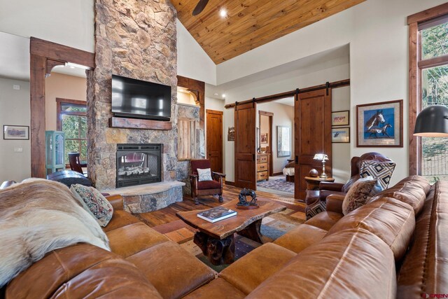 living room with a fireplace, a barn door, high vaulted ceiling, wooden ceiling, and wood finished floors