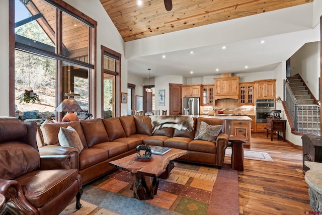 living area featuring high vaulted ceiling, recessed lighting, light wood finished floors, and stairs