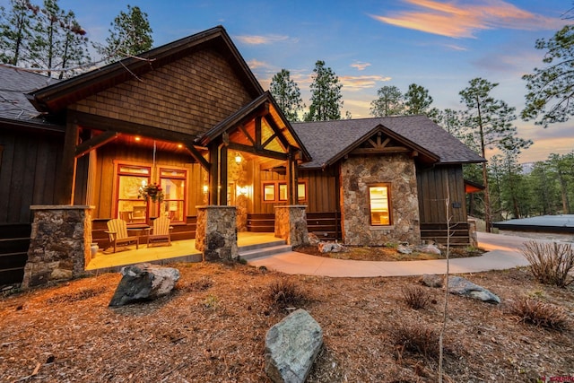 craftsman house with roof with shingles, covered porch, and stone siding