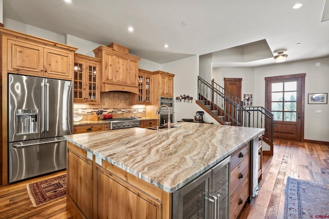 kitchen featuring appliances with stainless steel finishes, light stone counters, a sink, wine cooler, and wood-type flooring