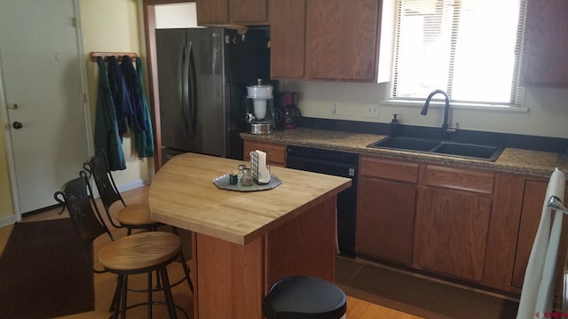 kitchen featuring black dishwasher, a sink, freestanding refrigerator, a breakfast bar, and butcher block countertops