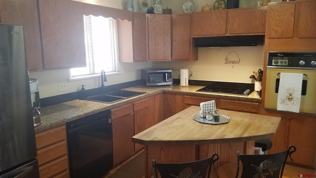 kitchen with wooden counters, black appliances, under cabinet range hood, brown cabinets, and a sink