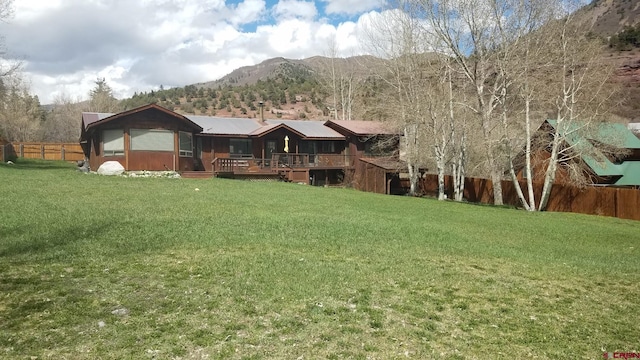 rear view of house with a yard, a deck with mountain view, and fence