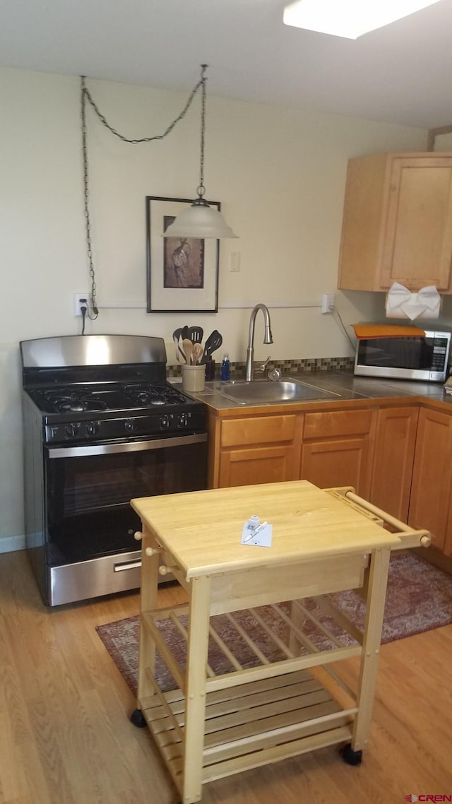 kitchen featuring a sink, light wood-type flooring, appliances with stainless steel finishes, and dark countertops