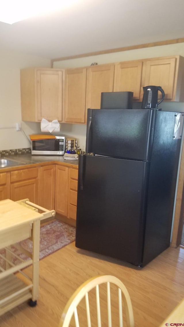 kitchen with light brown cabinets, a sink, freestanding refrigerator, stainless steel microwave, and light wood-style flooring