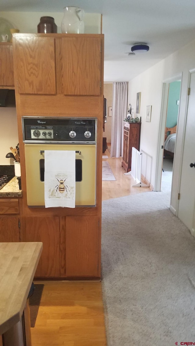 kitchen with white oven, brown cabinets, light wood-type flooring, and black cooktop
