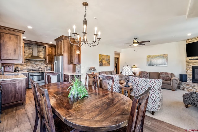 dining room with recessed lighting, a stone fireplace, ceiling fan with notable chandelier, and wood finished floors