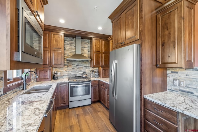 kitchen with tasteful backsplash, wall chimney range hood, light wood-style floors, appliances with stainless steel finishes, and a sink