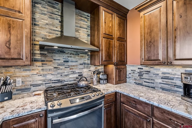 kitchen with stainless steel gas stove, decorative backsplash, wall chimney exhaust hood, and light stone countertops