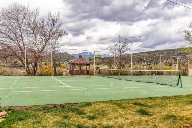 view of tennis court with a mountain view, fence, and a gazebo
