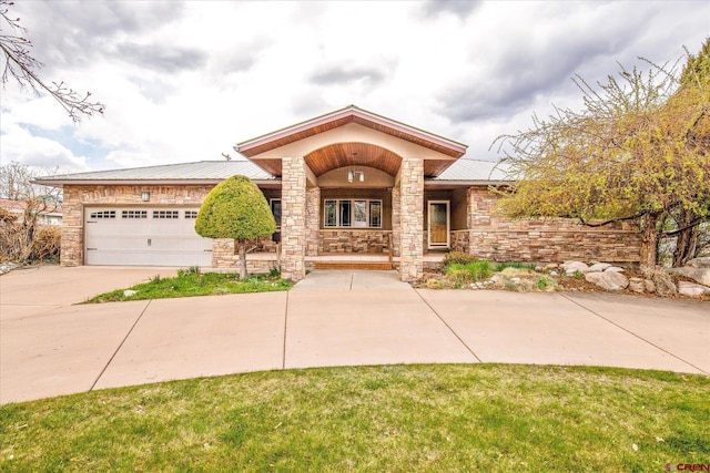 view of front of home with an attached garage, driveway, stone siding, a porch, and metal roof