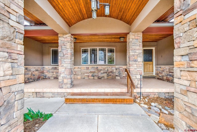doorway to property featuring stucco siding, a porch, and stone siding