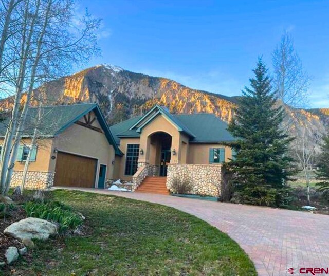 138 Silver Sage Dr, Crested Butte, CO 81224 - ranch-style home featuring stucco siding, stone siding, a front yard, a mountain view, and a garage