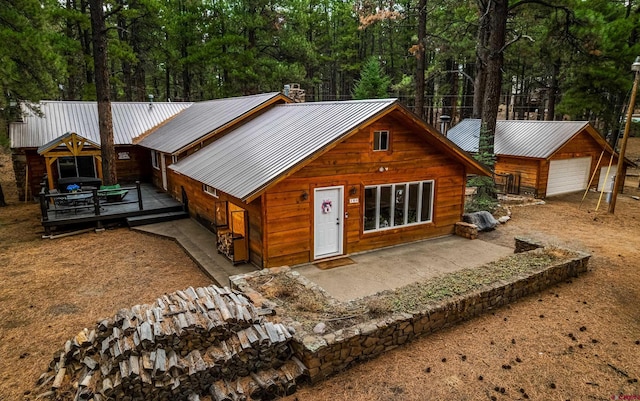 chalet / cabin with a wooden deck, a patio, a detached garage, and metal roof