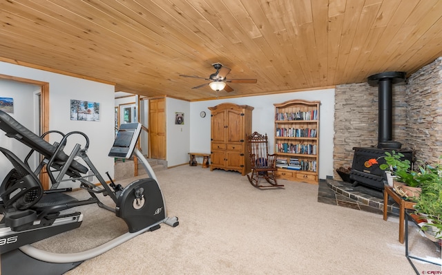 exercise room with wood ceiling, carpet flooring, a ceiling fan, and a wood stove