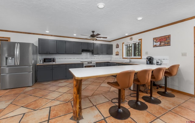 kitchen featuring under cabinet range hood, stainless steel appliances, a breakfast bar, ornamental molding, and a peninsula