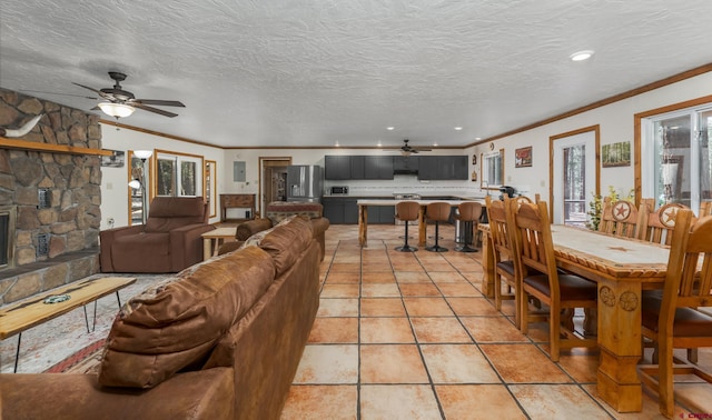 living area with ceiling fan, crown molding, a stone fireplace, and light tile patterned floors