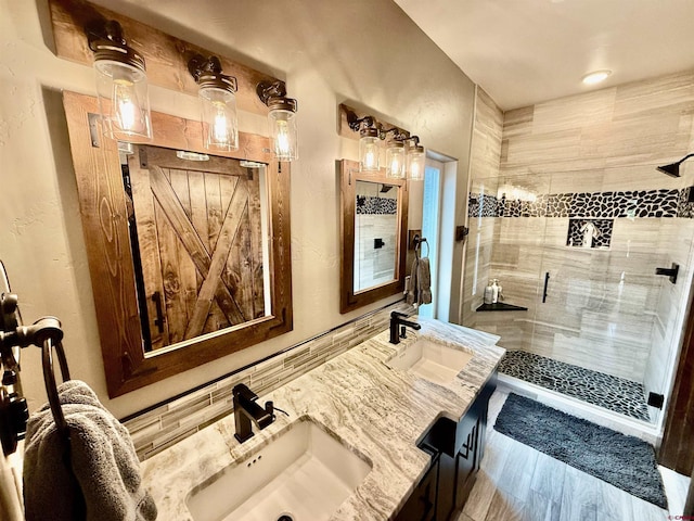 full bathroom with wood finished floors, a sink, double vanity, and a stall shower