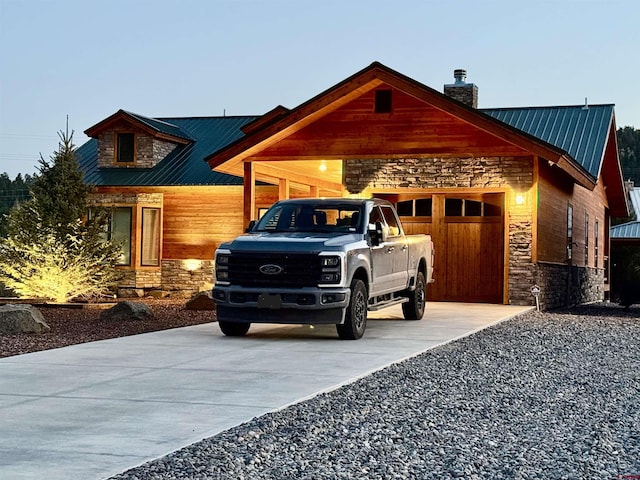 view of front of house with stone siding, a chimney, metal roof, concrete driveway, and an attached garage