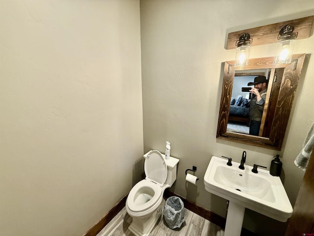 bathroom featuring wood finished floors, toilet, baseboards, and a sink
