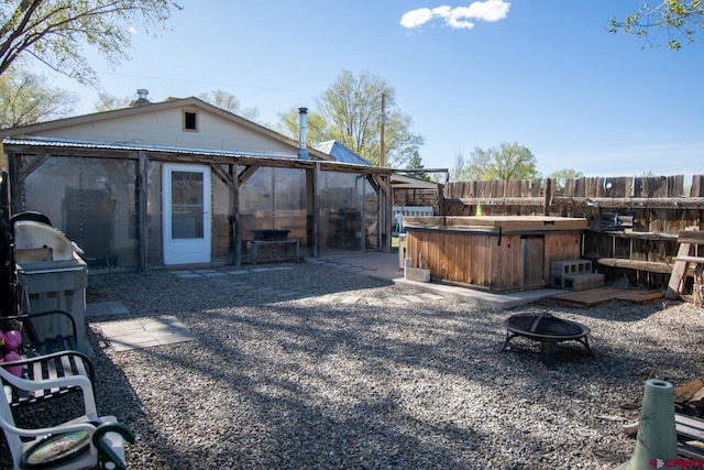view of yard featuring an outdoor fire pit, fence, a hot tub, a patio, and a sunroom