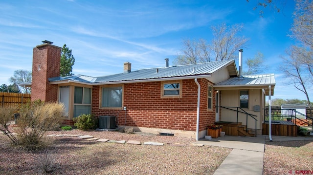 back of house with a chimney, brick siding, fence, metal roof, and central air condition unit