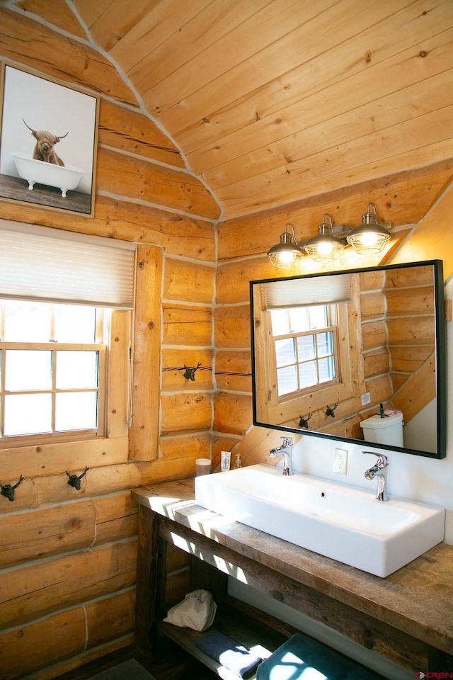 bathroom with rustic walls, vaulted ceiling, toilet, a sink, and wood ceiling