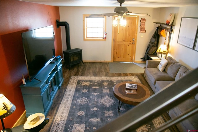 living room with wood finished floors, a wood stove, a ceiling fan, and baseboards