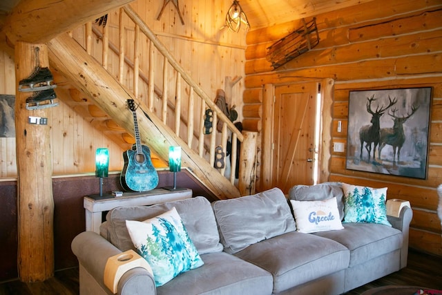 living room featuring log walls, vaulted ceiling, wood walls, and stairway