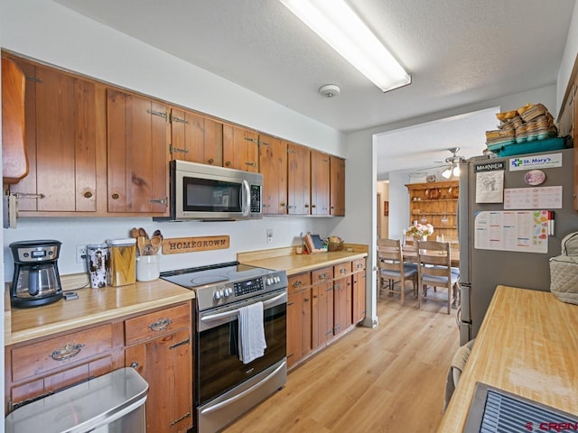 kitchen with light wood-style flooring, a textured ceiling, a ceiling fan, brown cabinetry, and appliances with stainless steel finishes