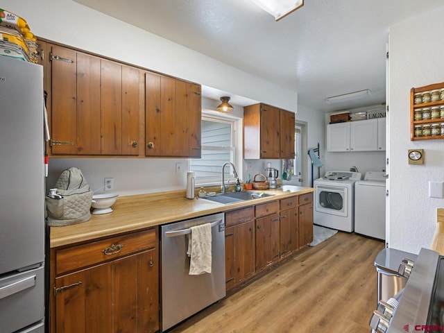 kitchen with a sink, separate washer and dryer, light wood-style floors, light countertops, and appliances with stainless steel finishes