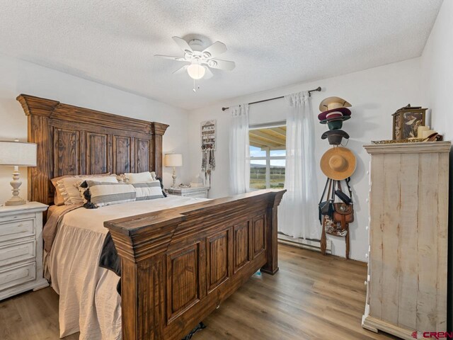bedroom with light wood finished floors, a ceiling fan, a textured ceiling, and baseboard heating