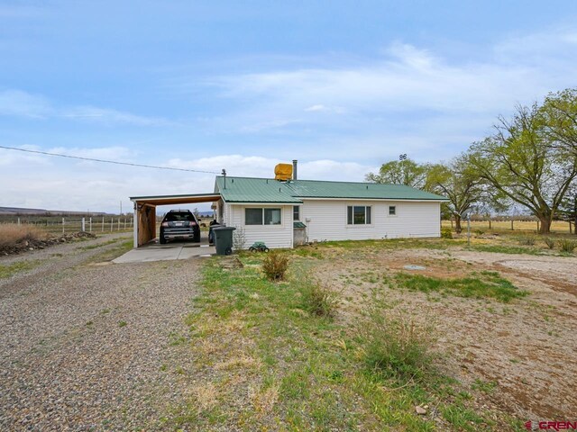 back of property featuring gravel driveway, an attached carport, fence, and metal roof