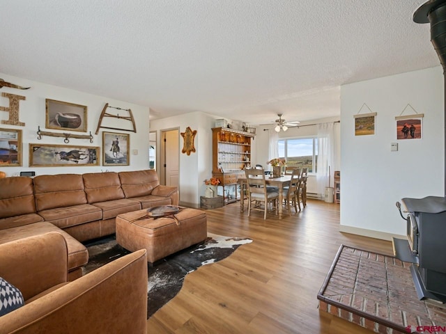 living area with a ceiling fan, wood finished floors, a textured ceiling, a baseboard heating unit, and a wood stove