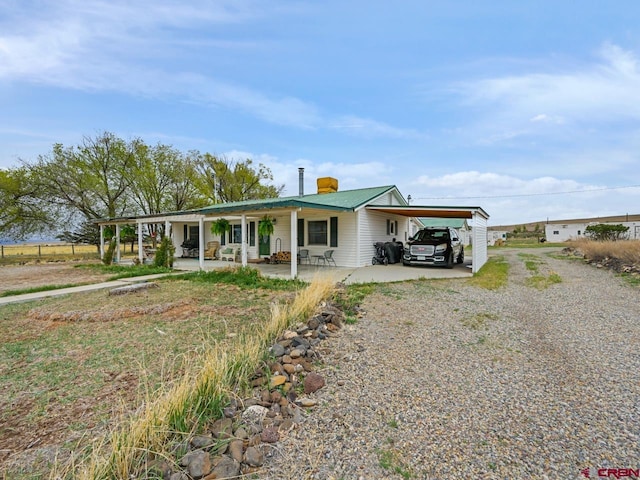 view of front facade with gravel driveway, a chimney, metal roof, and an attached carport