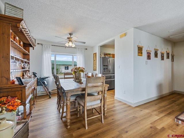 dining area featuring light wood-style floors, a textured ceiling, baseboards, and ceiling fan
