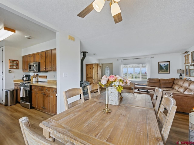 dining space featuring ceiling fan, light wood-style flooring, a textured ceiling, and a wood stove
