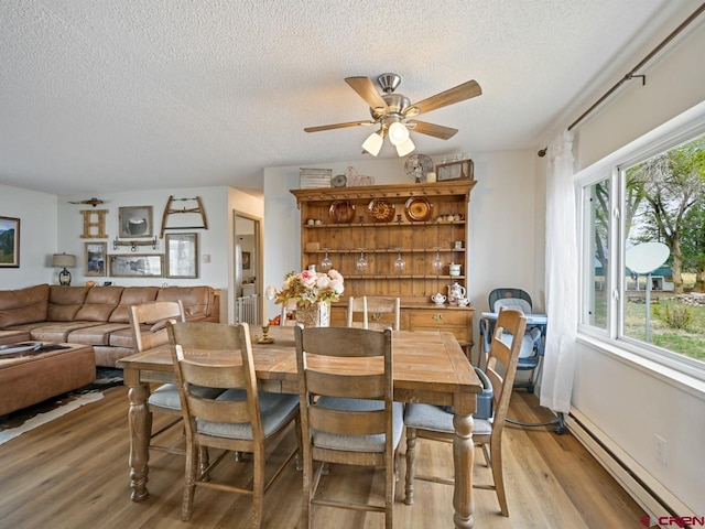 dining room with light wood-style floors, a wealth of natural light, a textured ceiling, baseboard heating, and ceiling fan