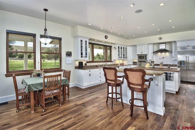 3575 E Rd, Palisade, CO 81526 - kitchen with wall chimney range hood, dark countertops, built in appliances, dark wood-style floors, and a kitchen island
