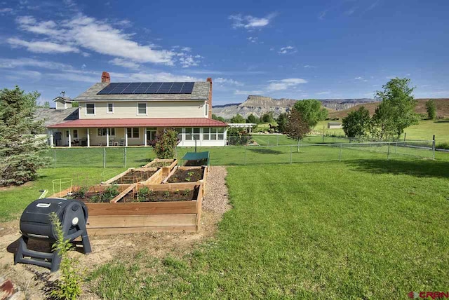 3575 E Rd, Palisade, CO 81526 - rear view of house with roof mounted solar panels, a lawn, a vegetable garden, and a chimney